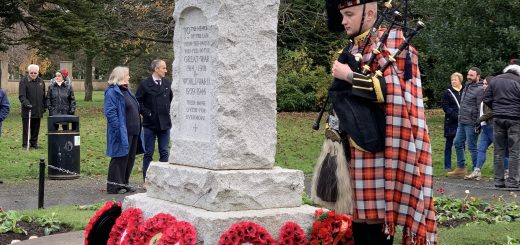 Piper in full regalia stands by the stone war memorial at Newtongrange