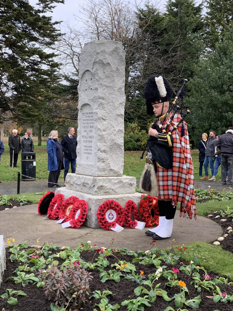 Piper in full regalia stands by the stone war memorial at Newtongrange